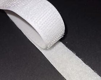 May include: A roll of white hook and loop fastener tape. The tape is unrolled on a black surface.