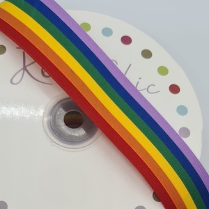 May include: Rainbow ribbon with red, orange, yellow, green, blue, and purple stripes. The ribbon is rolled up on a white spool with colorful dots.