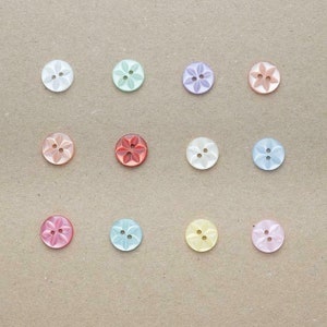 May include: Assortment of 12 colourful buttons with a five-pointed star design. The buttons are arranged in a grid pattern on a brown background.