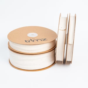 May include: Three spools of white cotton twill tape, each wrapped in brown cardboard with the word "trimz" printed on the cardboard.