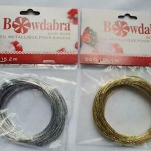 Puede incluir: Dos carretes de alambre metálico para hacer lazos. Los carretes están etiquetados "Bowdabra Bow Wire Fil Metallique Pour Boucle" y tienen 50 pies (15,2 metros) de largo. Un carrete es plateado y el otro es dorado.