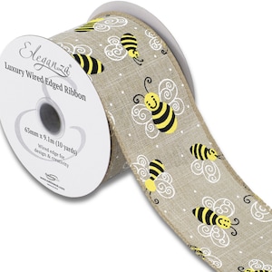 Op de afbeelding: Een rol beige draad-gekanteld lint met een herhalend patroon van gele en zwarte cartoon-bijen op een witte achtergrond met witte stippen. Het lint is 63 mm breed en 9,1 m lang (10 yards). Het label luidt "Eleganza Luxury Wired Edged Ribbon".