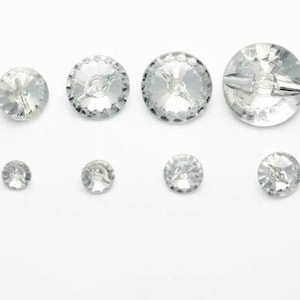 Op de afbeelding: Assortiment van heldere kristallen knopen in verschillende maten. De knopen hebben een facetgeslepen ontwerp en een viergaatsconfiguratie.