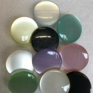 May include: Assortment of ten round, flat, iridescent buttons in various colours, including white, black, green, purple, and pink.