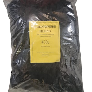 Puede incluir: Una bolsa de plástico negra llena de 400 gramos de relleno de fibra hueca. La bolsa tiene una etiqueta amarilla que dice "Hollowfibre Filling", "100% Viscose Random Polyester Filling", "Washable Supreme Quality", "400g", "All Purpose Stuffing", "Suitable for Toys & Cushions & Crafts", "Manufactured to", "BS5852 PT 2 1993".