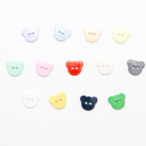 May include: Assortment of 12 colourful bear-shaped buttons. The buttons are made of plastic and have two holes. The colours include light blue, pink, light green, red, white, yellow, dark blue, and green.