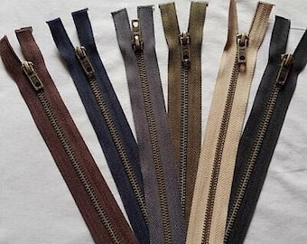 May include: Assortment of eight zipper closures with antique brass sliders and teeth. The zippers are in various colors, including brown, beige, gray, and black.