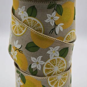 May include: A roll of beige fabric ribbon with a lemon print. The ribbon features yellow lemon slices, green leaves, and white flowers.