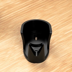 May include: Black plastic wall mount designed to hold a device, such as a phone or speaker, in a vertical position.