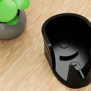 May include: A black plastic holder for a charging cable. The holder has a curved shape and a small opening on the side.