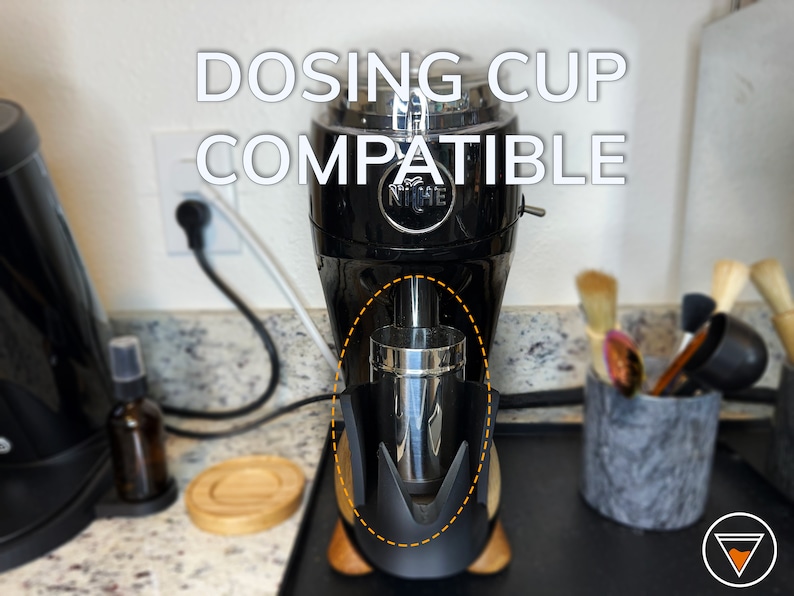 May include: A black Niche Zero coffee grinder with a stainless steel dosing cup attached to the bottom. The text "DOSING CUP COMPATIBLE" is written in white letters on the grinder.