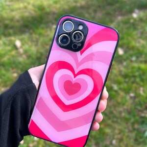 May include: A pink and red phone case with a swirling heart design. The case has a black border and a camera lens cutout.