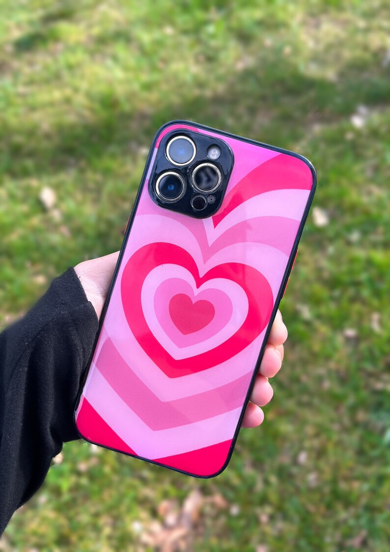 May include: A pink and red phone case with a swirling heart design. The case has a black border and a camera lens cutout.
