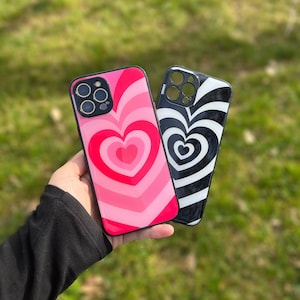 May include: Two phone cases with a heart design. One case is pink with a red heart and the other is black and white with a white heart.