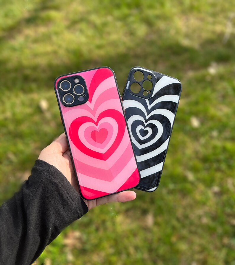 May include: Two phone cases with a heart design. One case is pink with a red heart and the other is black and white with a white heart.