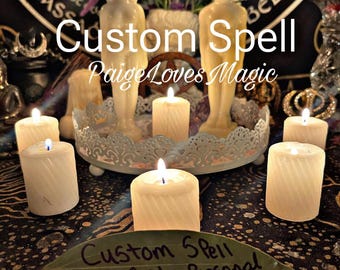 May include: A close-up of a custom spell kit with white candles, a leaf with the words "Custom Spell Manifest Personal Desires" written on it, and a background of a black and white patterned fabric.