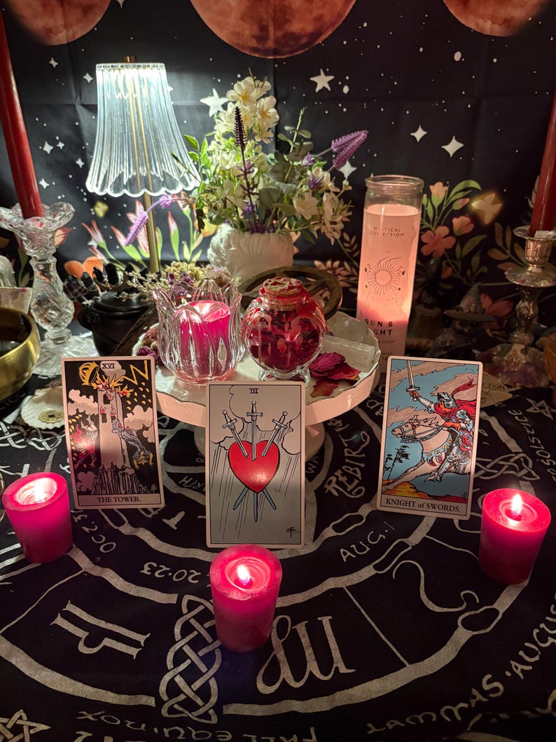 May include: A mystical scene featuring tarot cards, candles, and floral arrangements. The cards include "The Tower", "Three of Swords", and "Knight of Swords". Pink candles and a decorative lamp add to the ambiance. A black cloth with zodiac symbols is the backdrop.