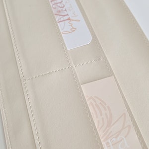 May include: A cream-colored leather wallet with multiple card slots. The wallet has a stitched design and features two cards with floral designs and the text "Aura" and "@aura".