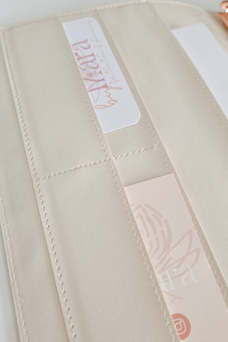 May include: A cream-colored leather wallet with multiple card slots. The wallet has a stitched design and features two cards with floral designs and the text "Aura" and "@aura".