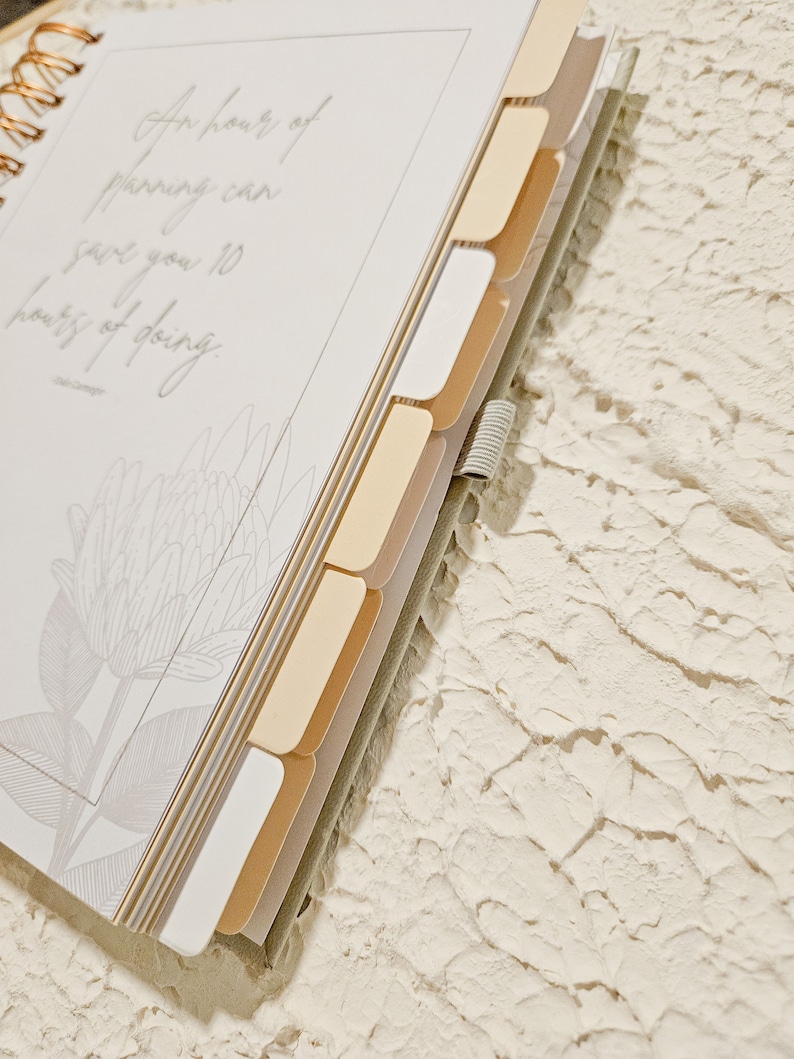 May include: A white planner with a gold spiral binding and gold tabs. The planner has a quote on the front that reads "An hour of planning can save you 10 hours of doing."