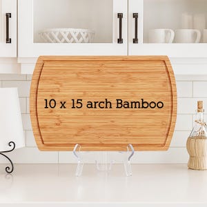 May include: A rectangular bamboo cutting board with a juice groove, measuring 10 x 15 inches. The text "10 x 15 arch Bamboo" is printed on the board. The board is displayed on a clear plastic stand.