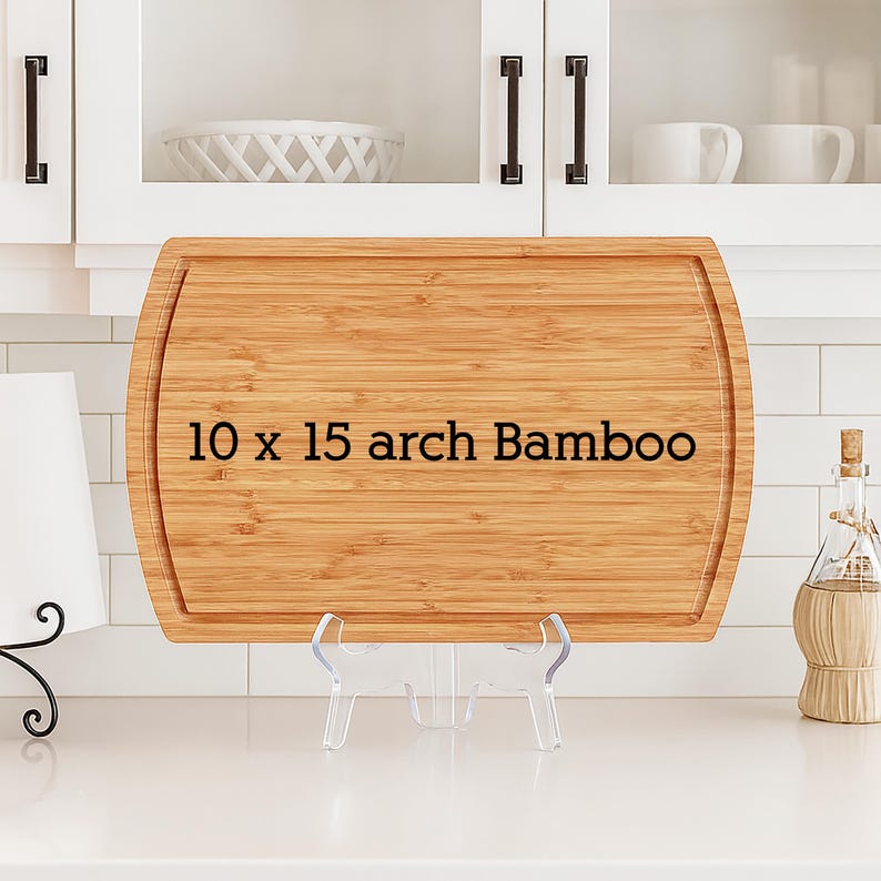 May include: A rectangular bamboo cutting board with a juice groove, measuring 10 x 15 inches. The text "10 x 15 arch Bamboo" is printed on the board. The board is displayed on a clear plastic stand.
