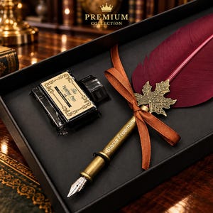 Puede incluir: Una pluma estilográfica de color burdeos con un adorno de hoja de arce de metal dorado y una cinta marrón, personalizada con el nombre Stacia Freeman. El set incluye un tintero negro con la etiqueta The Feather Pen en una caja negra.