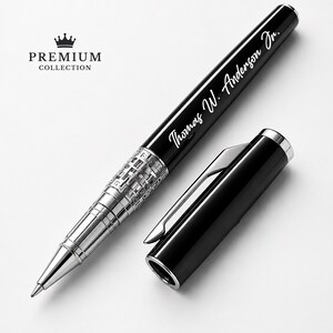 Puede incluir: Un bol&iacute;grafo negro y plateado con el texto "Thomas W. Anderson Jr." grabado en el cuerpo. El bol&iacute;grafo tiene una punta plateada y una banda plateada decorativa. La tapa del bol&iacute;grafo est&aacute; a un lado. Las palabras "PREMIUM COLLECTION" est&aacute;n impresas encima de una corona.