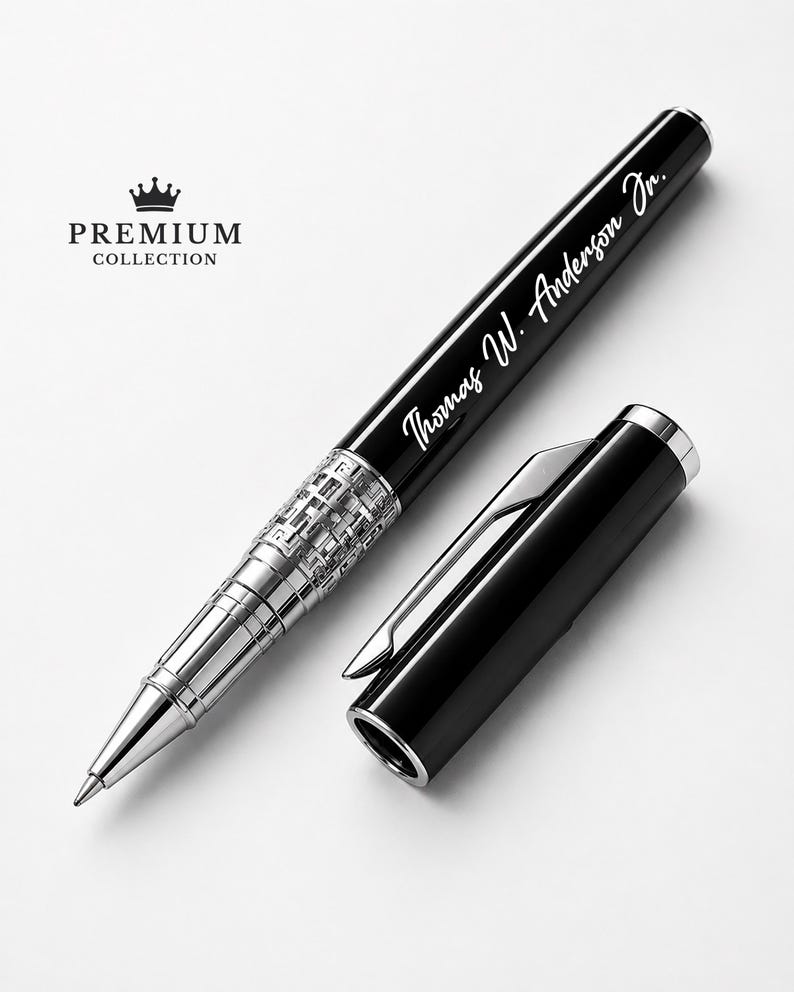 Puede incluir: Un bol&iacute;grafo negro y plateado con el texto "Thomas W. Anderson Jr." grabado en el cuerpo. El bol&iacute;grafo tiene una punta plateada y una banda plateada decorativa. La tapa del bol&iacute;grafo est&aacute; a un lado. Las palabras "PREMIUM COLLECTION" est&aacute;n impresas encima de una corona.