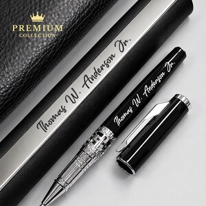 Puede incluir: Un bol&iacute;grafo negro con detalles plateados y la inscripci&oacute;n "Thomas W. Anderson Jr." se muestra junto a su estuche. La tapa del bol&iacute;grafo est&aacute; quitada, revelando la punta. El estuche es negro con una franja plateada y las palabras "Premium Collection".