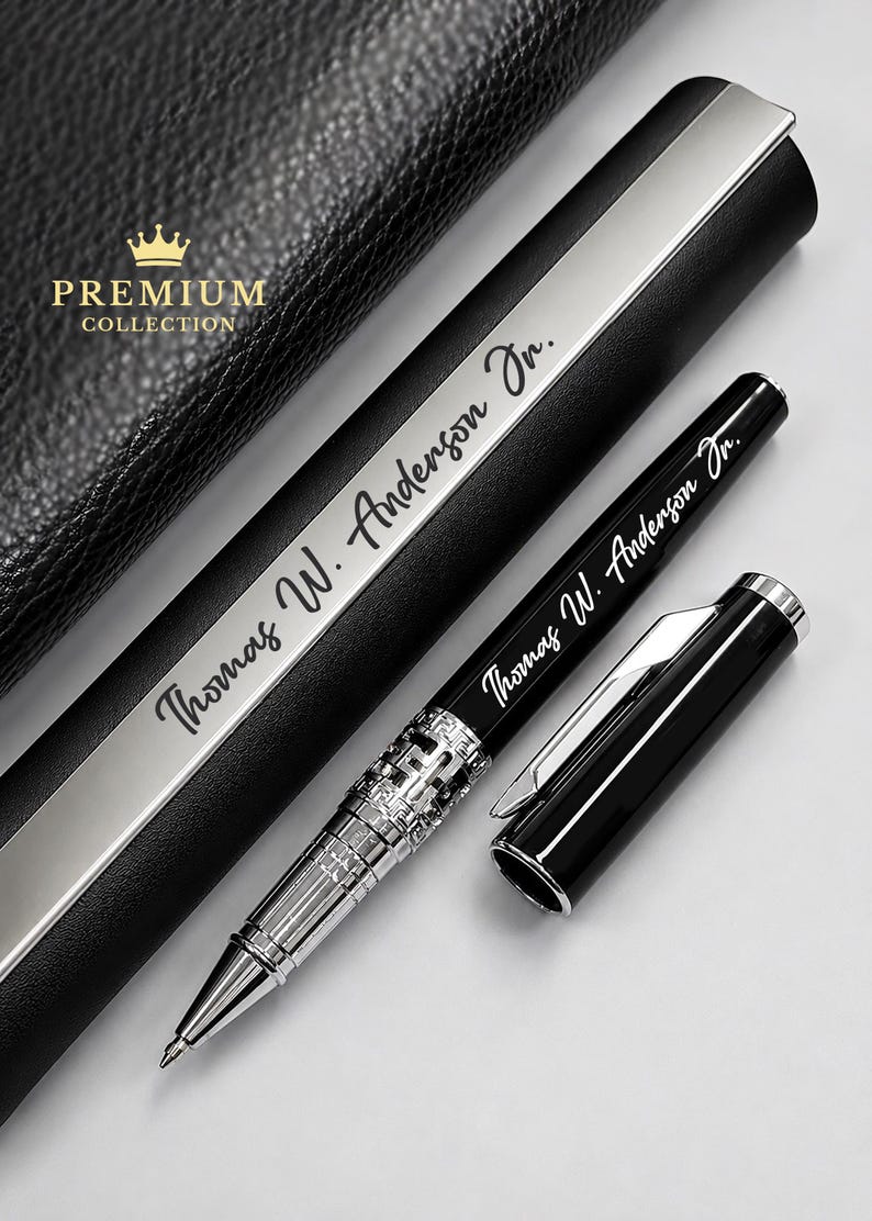 Puede incluir: Un bol&iacute;grafo negro con detalles plateados y la inscripci&oacute;n "Thomas W. Anderson Jr." se muestra junto a su estuche. La tapa del bol&iacute;grafo est&aacute; quitada, revelando la punta. El estuche es negro con una franja plateada y las palabras "Premium Collection".