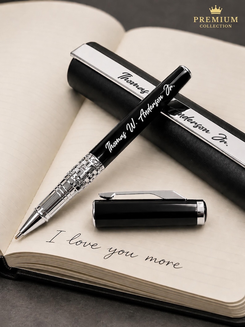 Puede incluir: Un bol&iacute;grafo negro y plateado con la inscripci&oacute;n "Thomas W. Anderson Jr." se muestra en un cuaderno abierto. El bol&iacute;grafo est&aacute; junto a su estuche, que tambi&eacute;n tiene el nombre grabado. El cuaderno dice "I love you more."