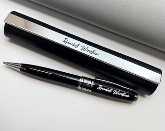 Può includere: Una penna nera con dettagli argentati e il nome "Randall Wordlaw" inciso sul fusto. Accanto, un astuccio per penna nero abbinato con la parte superiore argentata e lo stesso nome inciso.