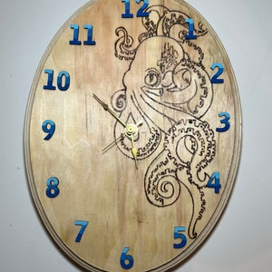 Op de afbeelding: Een houten klok met een octopus-ontwerp. De wijzerplaat van de klok is ovaalvormig en heeft blauwe cijfers. De octopus bevindt zich in het midden van de wijzerplaat en wordt omringd door zijn tentakels.