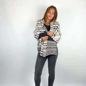 May include: A woman wearing a black and white striped scarf with a black long-sleeved shirt and dark gray jeans.