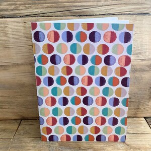 May include: A white card with a repeating pattern of colourful half circles. The circles are in shades of red, orange, yellow, green, blue, and purple. The background is white.