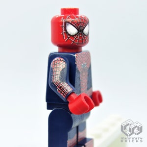 K&ouml;nnte beinhalten: Eine Lego Spider-Man-Minifigur. Die Figur hat einen roten Kopf mit wei&szlig;en Augen und einem schwarzen Netzdesign. Der Torso und die Arme sind dunkelblau mit einem roten und silbernen Netzmuster. Die H&auml;nde sind rot.