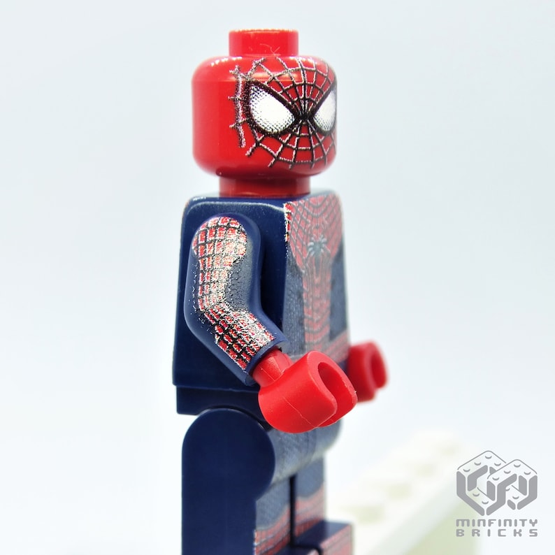 K&ouml;nnte beinhalten: Eine Lego Spider-Man-Minifigur. Die Figur hat einen roten Kopf mit wei&szlig;en Augen und einem schwarzen Netzdesign. Der Torso und die Arme sind dunkelblau mit einem roten und silbernen Netzmuster. Die H&auml;nde sind rot.