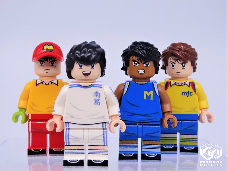 May include: Four minifigure toys of soccer players. The figures are wearing different colored jerseys with team logos and names. The figures are standing on a white surface.