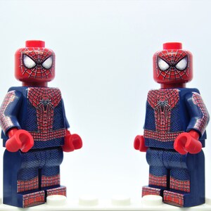 K&ouml;nnte beinhalten: Zwei Lego-Minifiguren von Spider-Man. Sie haben rote K&ouml;pfe mit wei&szlig;en Augen und Spinnennetzmustern. Die Kost&uuml;me sind blau mit roten Spinnennetzdesigns, roten Handschuhen und Stiefeln.
