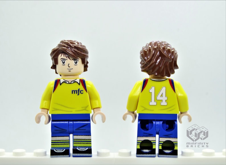 May include: A yellow and blue Lego minifigure wearing a soccer jersey with the text "mfc" on the front and the number "14" on the back.