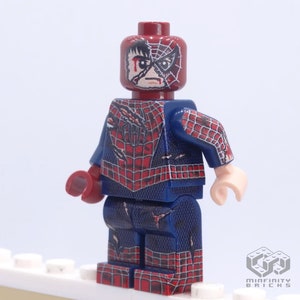 May include: A custom Lego minifigure of Spider-Man in a distressed state. The figure features a red and blue costume with a web design, and a damaged mask revealing a portion of the face. The figure is standing on a white surface.