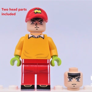 May include: A Lego minifigure with a yellow shirt, red pants, and a red cap with a green N on it. The minifigure has a printed face with a serious expression. Two head parts are included.