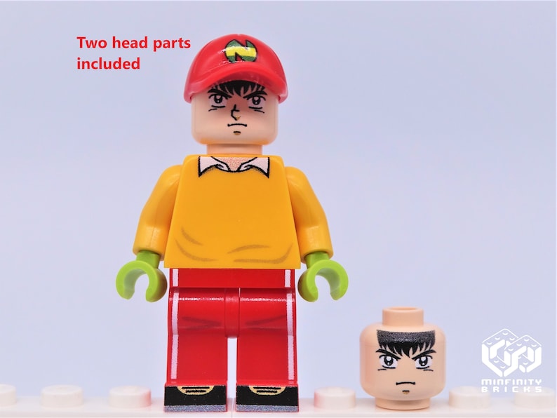 May include: A Lego minifigure with a yellow shirt, red pants, and a red cap with a green N on it. The minifigure has a printed face with a serious expression. Two head parts are included.