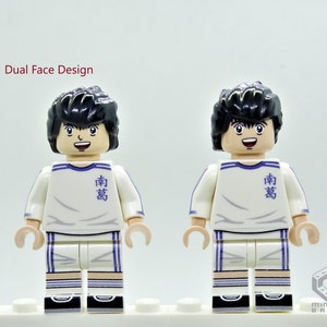 May include: A white and blue Lego minifigure with black hair and a smiling face. The minifigure is wearing a white jersey with blue stripes and the Japanese word "南葛" written on the front. The minifigure has a dual face design, with a second face showing a more serious expression.