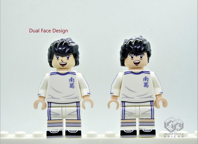 May include: A white and blue Lego minifigure with black hair and a smiling face. The minifigure is wearing a white jersey with blue stripes and the Japanese word "南葛" written on the front. The minifigure has a dual face design, with a second face showing a more serious expression.