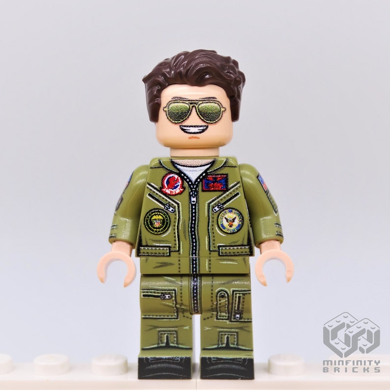 Puede incluir: Una minifigura Lego de un piloto que lleva un traje de vuelo verde con parches y gafas de sol. La minifigura tiene el pelo casta&ntilde;o y una cara sonriente.