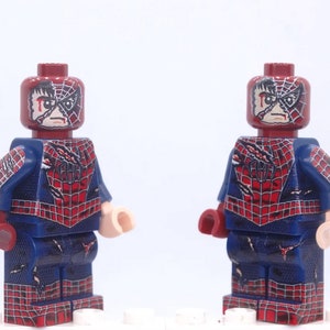 May include: Two Lego Spider-Man minifigures. Each figure has a dark red head with a distressed mask design and a blue and red suit. The suit features a spiderweb pattern and the word "AM" on the back. The figures are standing against a white background.
