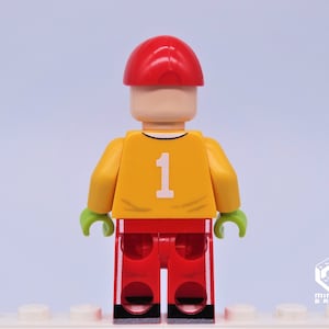 May include: A Lego minifigure wearing a red cap, yellow jersey with the number 1, red pants with white stripes, and green hands.