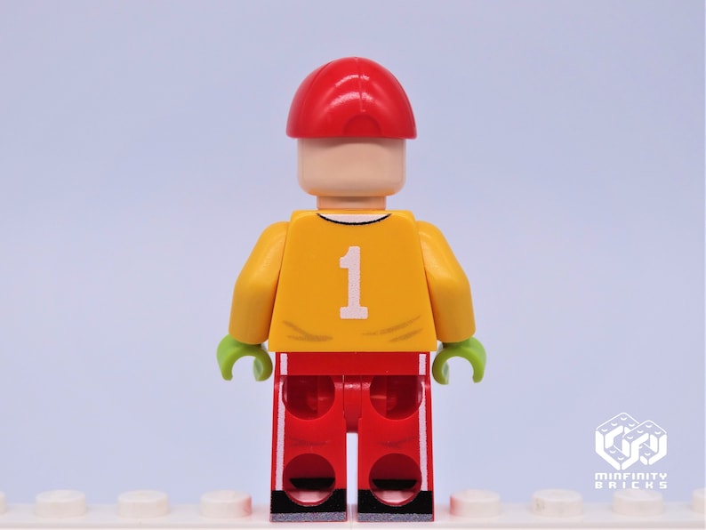 May include: A Lego minifigure wearing a red cap, yellow jersey with the number 1, red pants with white stripes, and green hands.